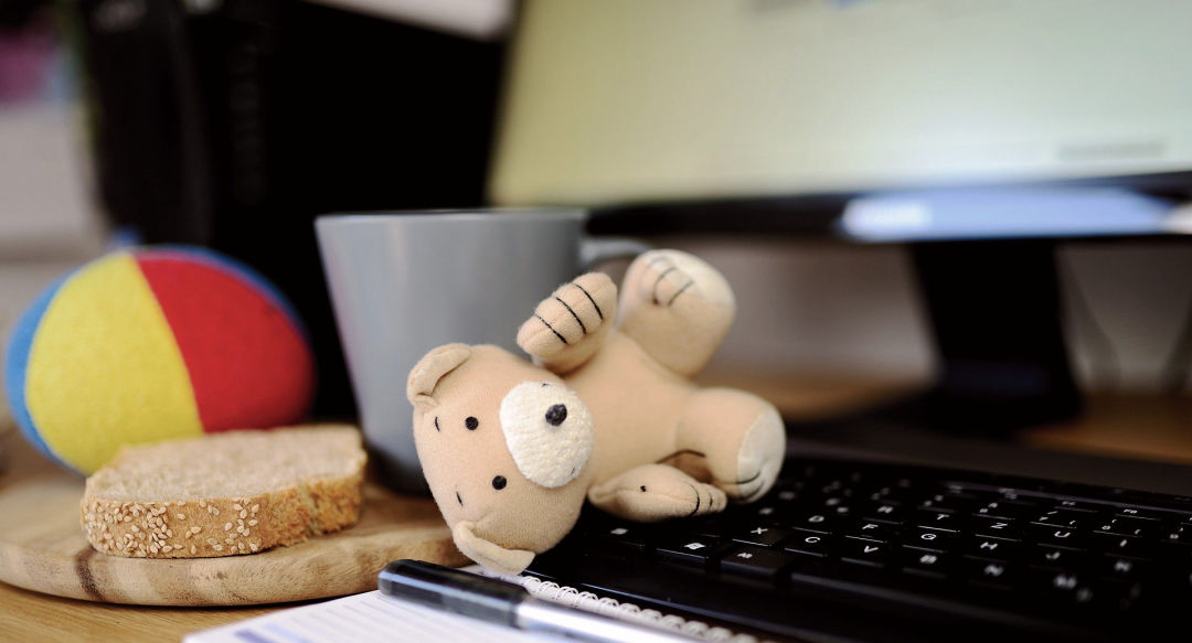 A teddy bear, and a small felt ball next to laptop