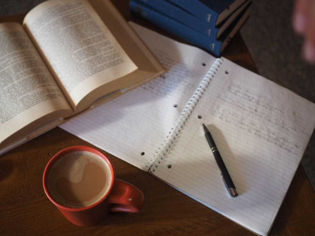 Open book and notebook with hot cup of coffee